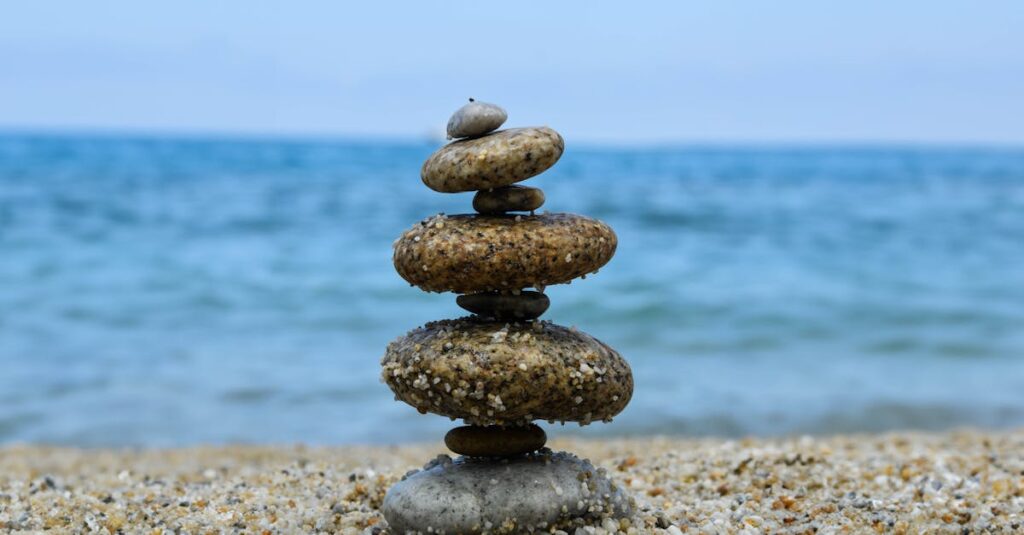 Balanced stones stacked on a sandy beach with a calm ocean backdrop, evoking tranquility and zen.
